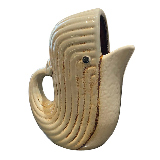 A ceramic whale-shaped pitcher with a cream-colored glaze and brown textured streaks, set on a dark granite countertop in a kitchen environment.