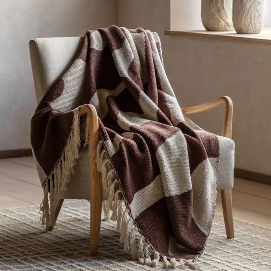 Brown and beige checkered blanket draped over a wooden chair in a room with neutral decor.