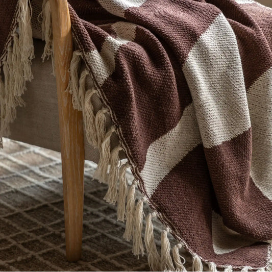 Brown and beige checkered blanket with tassels draped over a wooden chair.