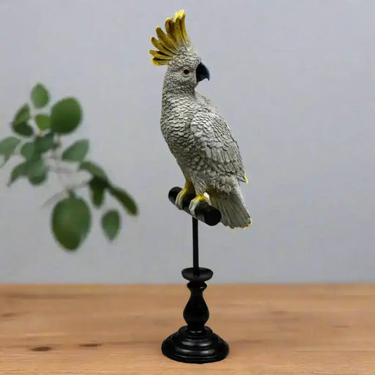 Gray parrot figurine with a yellow crest on a black stand against a white background