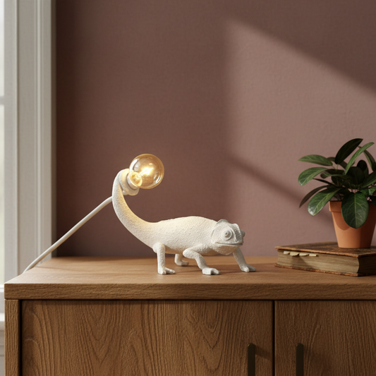Lamp shaped like a chameleon on a wooden surface with a plant in the background