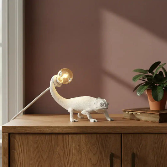 Lamp shaped like a chameleon on a wooden surface with a plant in the background