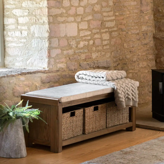 Wooden bench with storage baskets and folded blankets against a stone wall.