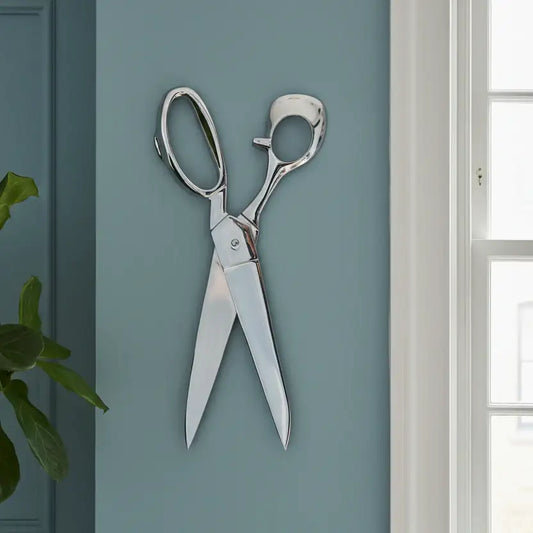 Silver scissors on a light blue wall with a plant and window in the background