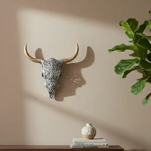 Decorative cow skull on a wall with a plant and small vase on a shelf below.