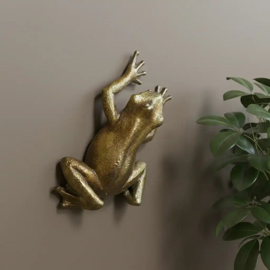 Gold frog sculpture on a textured stone wall