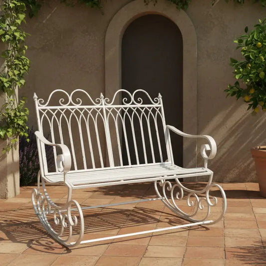 White metal garden bench on a patio with a building and plant in the background