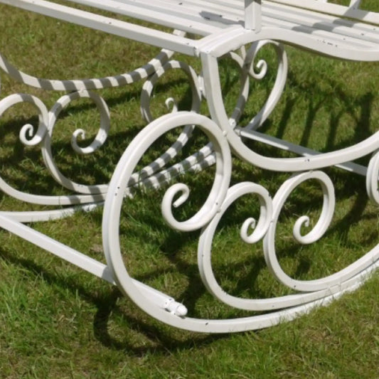 White metal garden bench with decorative scrollwork on a grassy background