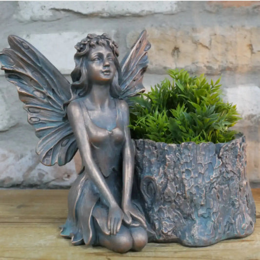 Bronze fairy statue with a planter shaped like a tree stump on a wooden surface.