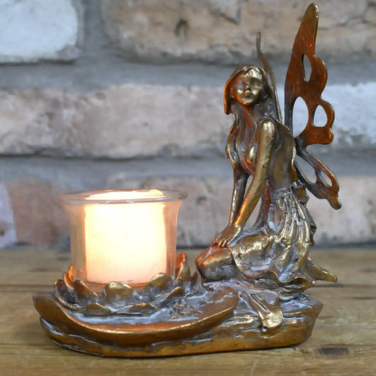 Bronze fairy figurine with a candle holder against a stone wall background