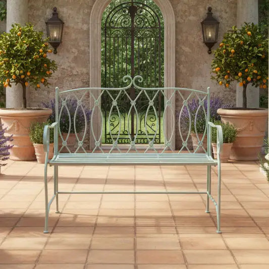 Decorative metal bench on a patio with potted plants and a garden gate in the background.