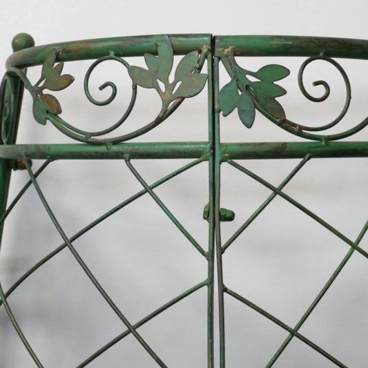 Close-up of a green metal gate with decorative leaves and swirls on a white background