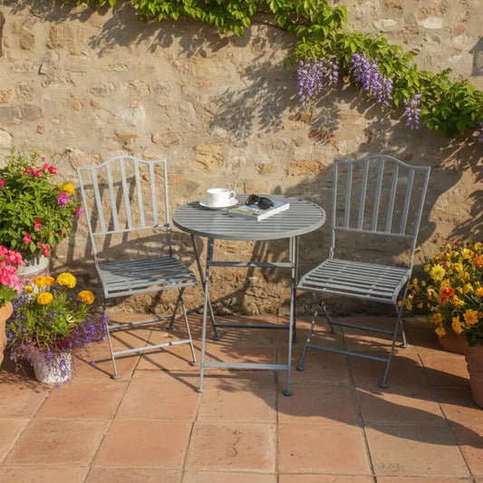 Outdoor patio set with table and chairs against a stone wall, surrounded by flowers.