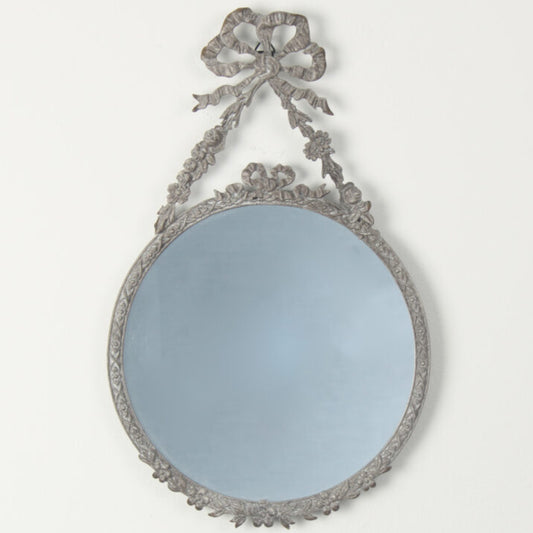Decorative round mirror with intricate frame and bow on a white background