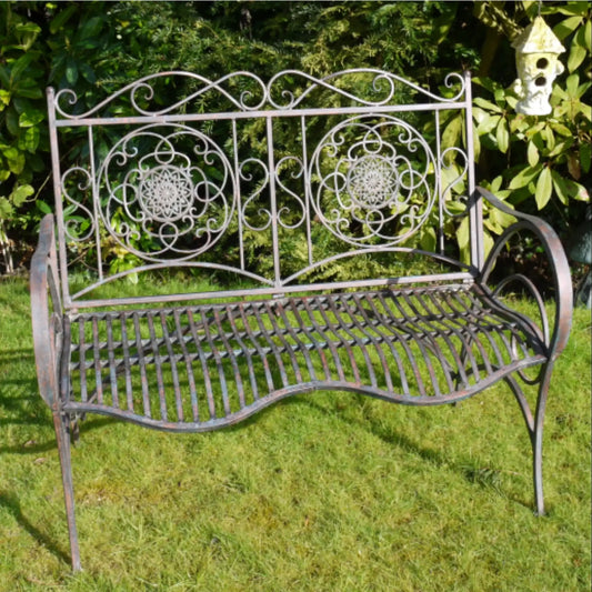 Decorative metal bench with intricate designs on a grassy area