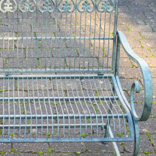 Decorative metal garden bench on a paved patio with greenery in the background