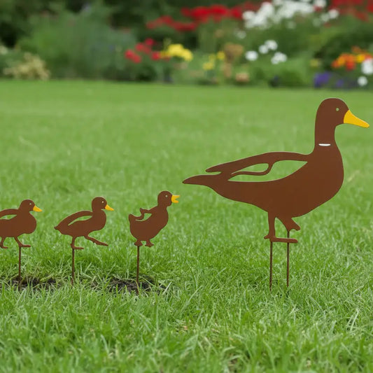 Metal duck family sculpture on grass with a garden in the background