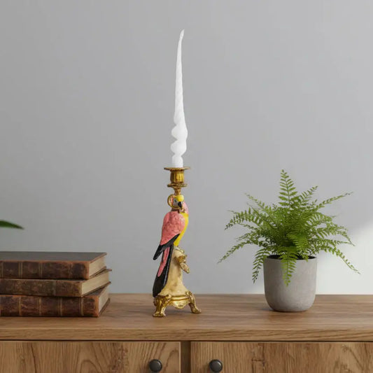 Decorative candlestick with parrot design on a wooden surface with books and a plant.