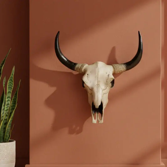 Bull skull with large horns on a brown wall next to a potted plant
