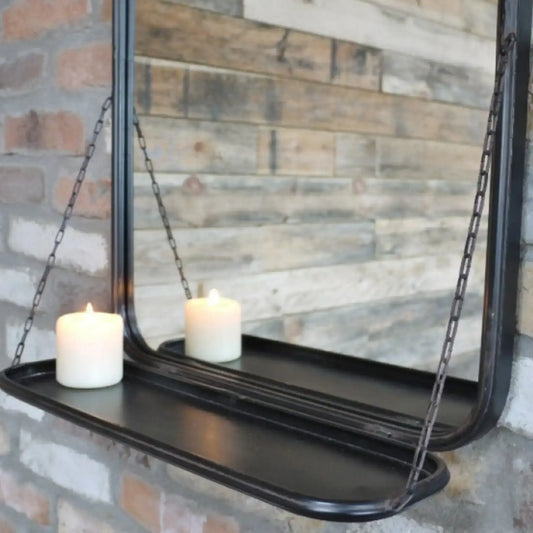Black hanging mirror with a shelf against a brick wall.