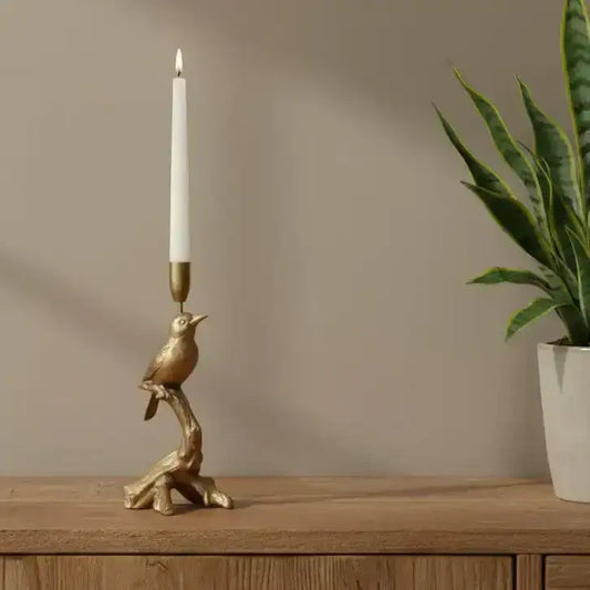 Gold bird-shaped candle holder with a white candle on a wooden surface next to a plant.