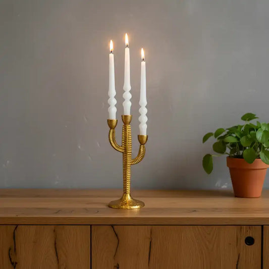 Gold candle holder with white candles on a wooden surface against a gray wall.
