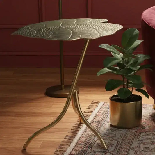 Decorative side table with leaf design against a teal wall.
