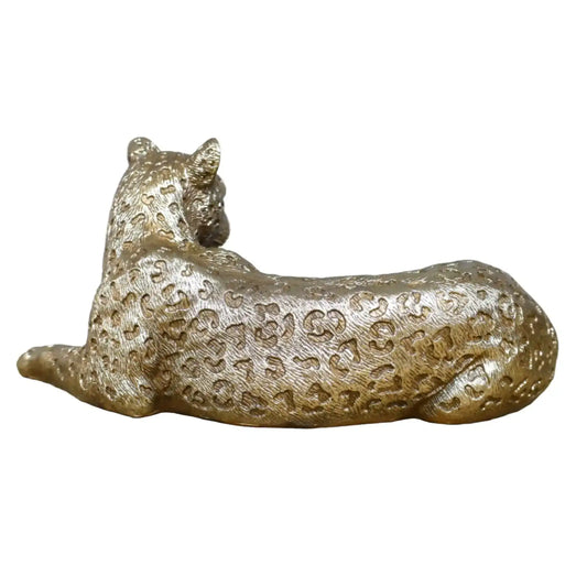 Gold leopard figurine on a wooden surface with a stone wall background