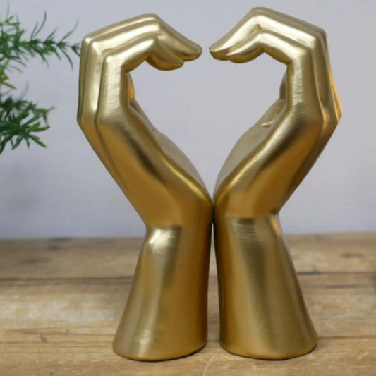Gold decorative hands sculpture on a wooden surface with a plant in the background
