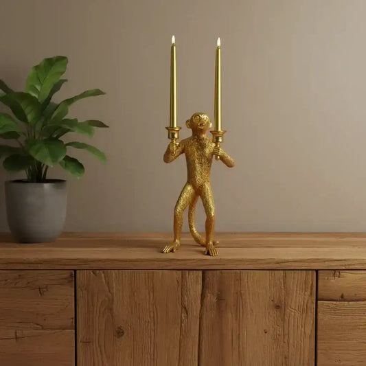 Gold monkey candle holder with two lit candles on a wooden surface next to a plant.