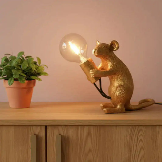 Gold rat figurine holding a light bulb with blurred lights in the background