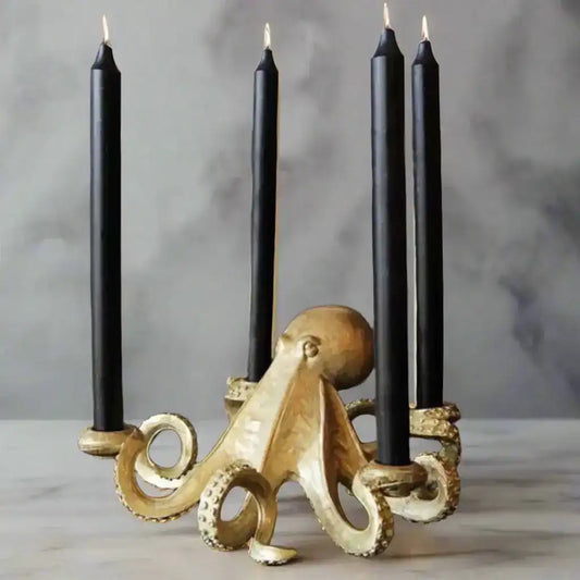 Gold octopus-shaped candle holder with four black candles on a gray background