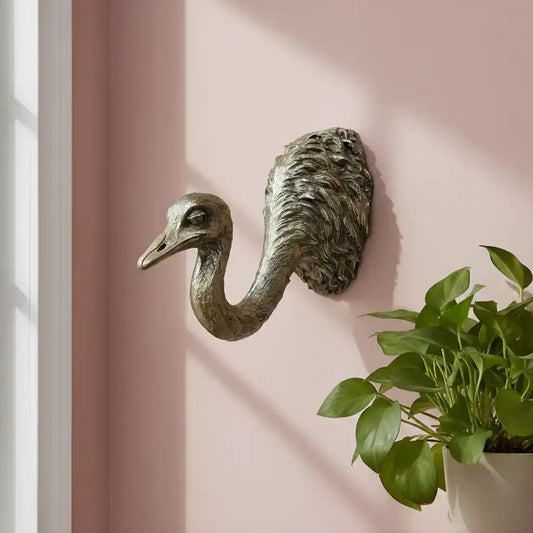 Bronze flamingo wall hook on a pink wall with a plant in the corner