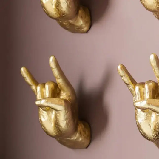 Gold hand gestures making the 'rock on' sign against a pink background