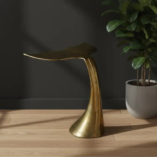 Gold leaf-shaped stool on a wooden floor with a dark wall and potted plant in the background