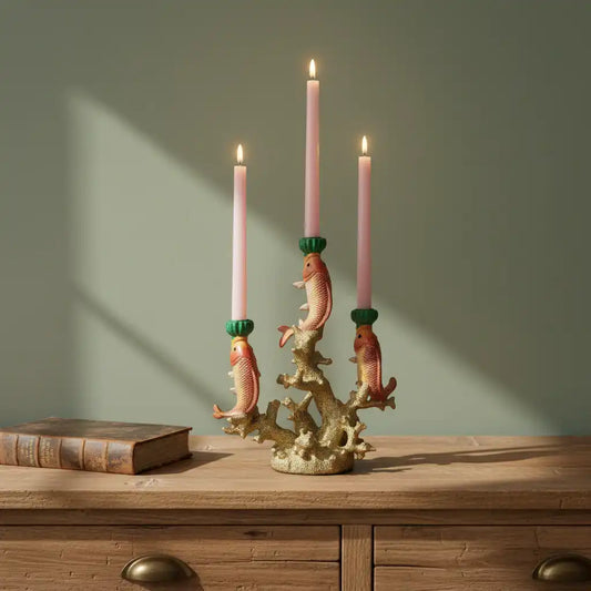 Decorative candle holder with fish design on a wooden surface against a green wall.