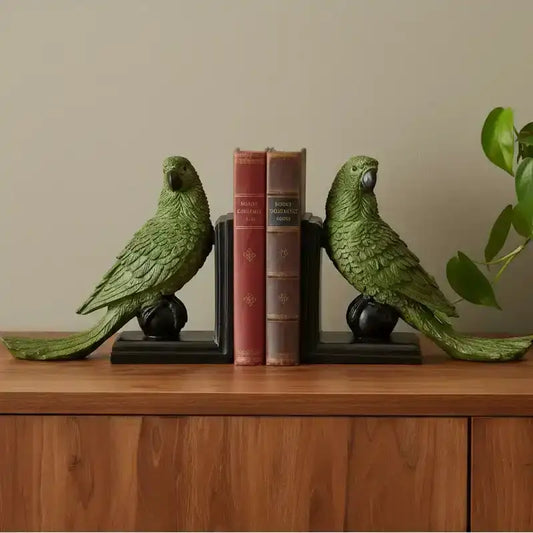 Green parrot bookends on a wooden surface with books between them against a beige wall.