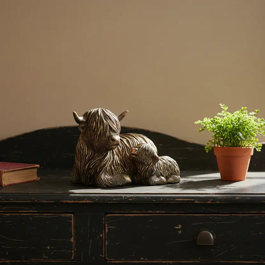 Statue of a mother bear with cubs on a wooden surface next to a potted plant.