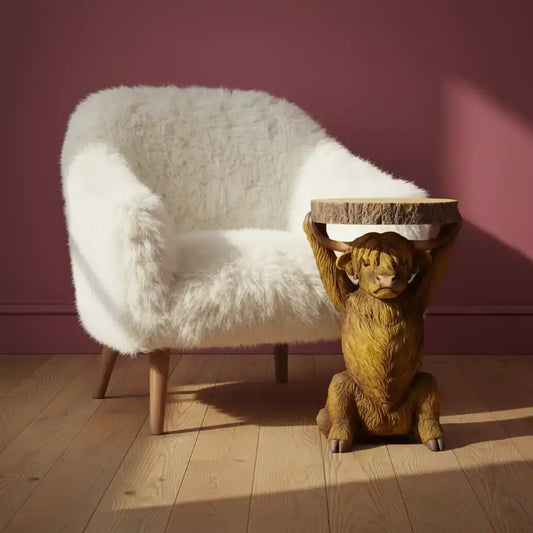 White fluffy chair and wooden lion table against a pink wall.