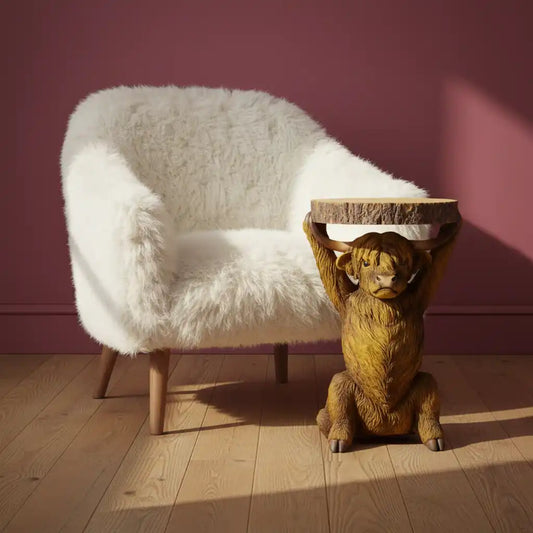 White fluffy chair and wooden lion table against a pink wall.