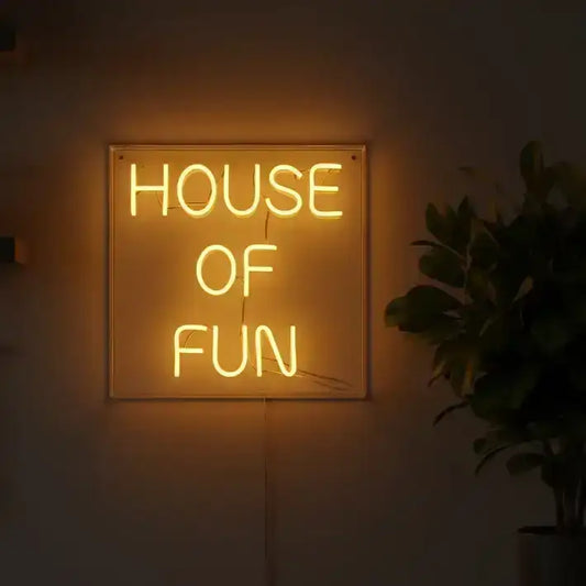 Neon sign reading 'HOUSE OF FUN' in a dimly lit room with a plant and kitchen utensils.