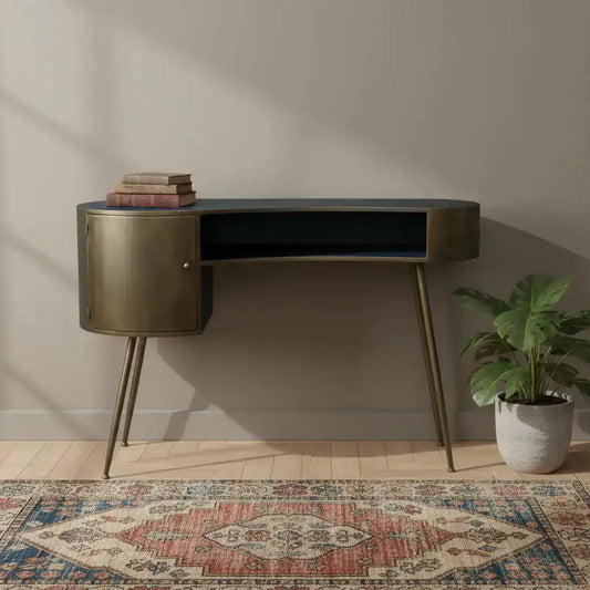 Modern desk with gold accents in a room with a patterned rug and plant.