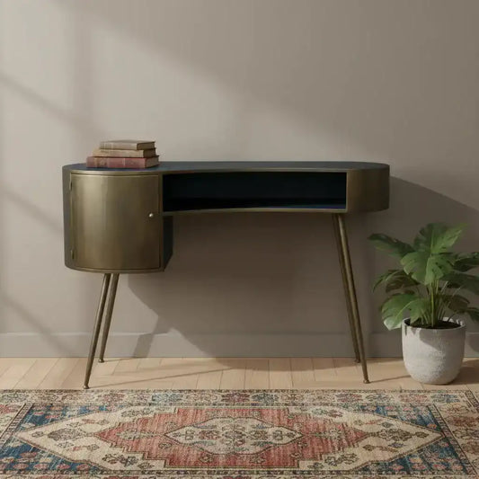 Modern desk with gold accents in a room with a patterned rug and plant.