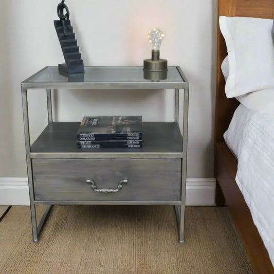Metal nightstand with glass top, books, and a lamp on a wooden floor.