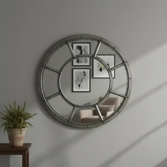 Round metallic wall mirror on a gray wall with a plant and chair in the foreground