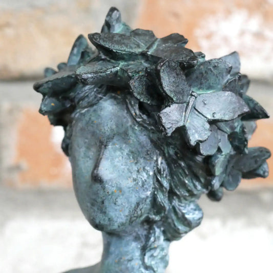 Bronze statue of a woman's head with leaves on her head against a blurred background