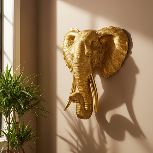 Gold elephant head wall decoration on a beige wall with a plant in the foreground.
