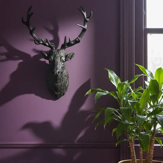 Decorative deer head mounted on a purple wall with plants in the foreground.
