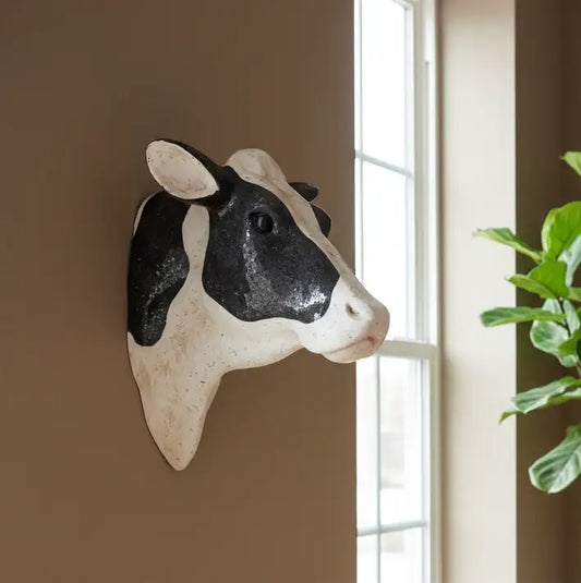 Decorative cow head wall art on a wall with a window and plant in the background