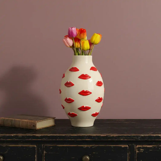 Vase with red lip designs and colorful tulips on a wooden surface against a purple wall
